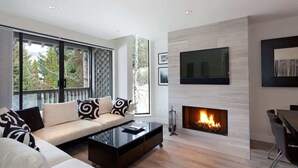 A modern living room with a sofa, coffee table, fireplace, and large windows.