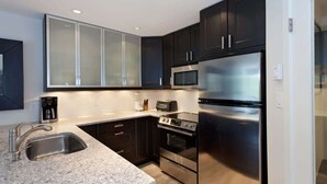 A modern kitchen with dark cabinets, stainless steel appliances, a granite countertop, and a built-in microwave.