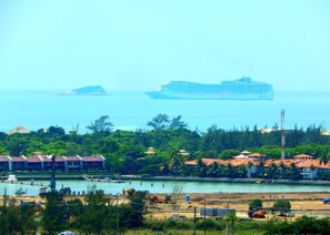 A coastal area with a large cruise ship in the distance, a marina with boats, and buildings with red roofs. - Pousada Preciosa (Búzios)