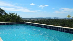 Piscina con borde de azulejos, rodeada de vegetación y un cielo despejado.