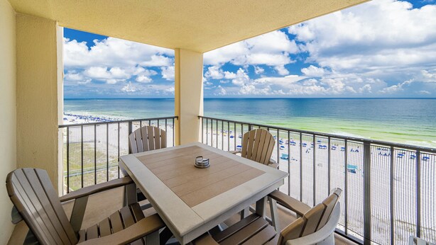 A balcony with a table and chairs overlooking a beach with a clear view of the ocean and sky. - 2 Bedroom on the BEACH! Phoenix III (Orange Beach)