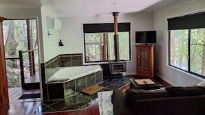 Une salle de bain moderne dotée d’une baignoire entourée de parois en verre, d’un poêle à bois et d’une grande fenêtre donnant sur l’extérieur.