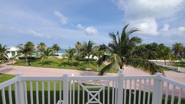 A resort with a white fence, palm trees, and a view of the ocean.