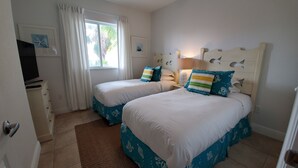 A bedroom with two beds, a window with curtains, a dresser, and wall art.