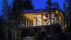 Ein modernes Blockhaus mit großen Glasfenstern, umgeben von dichtem Wald.