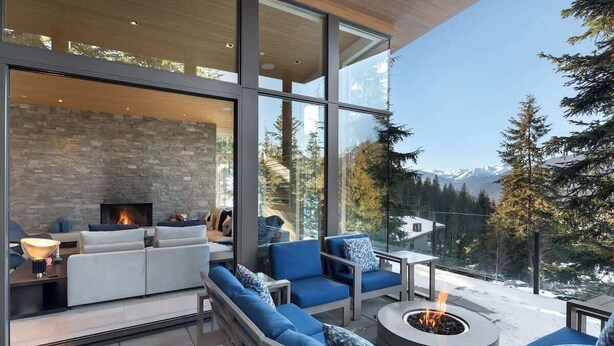 Ein modernes Wohnzimmer mit Kamin, großen Fenstern und Blick auf eine verschneite Berglandschaft.