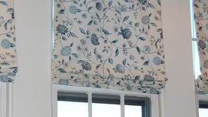 A window with a floral-patterned valance and a view of a body of water with boats.