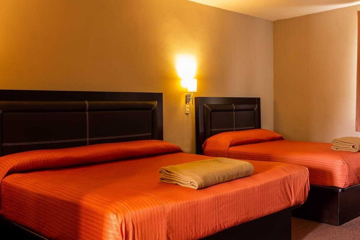 Habitació d'hotel amb dos llits, cadascun amb capçalera, i un llit amb almoada.