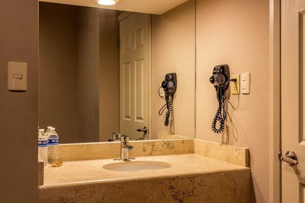 A bathroom with a sink, mirror, hairdryer, and a door.
