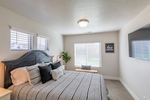 Quarto com cama, mesa de cabeceira e janela com persianas.