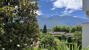 Une maison avec un toit en tuiles, entourée d’une végétation luxuriante et avec des montagnes en arrière-plan.