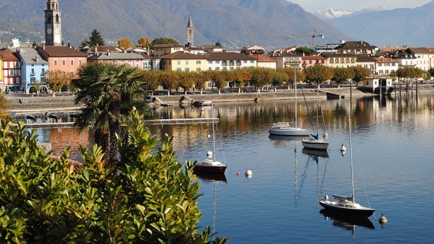 Une ville côtière avec des bateaux, un beffroi et des montagnes en arrière-plan.