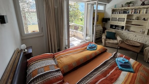 Une chambre à coucher comprenant un lit, une chaise, une bibliothèque et un balcon avec des rideaux.