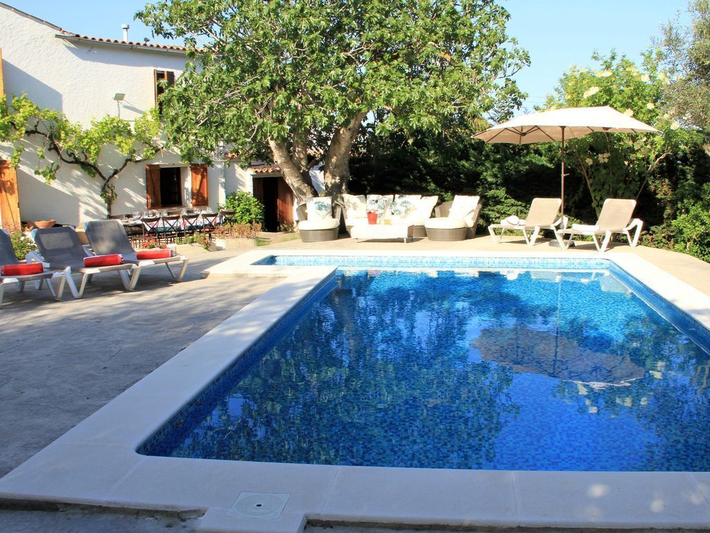 A swimming pool with lounge chairs and umbrellas, surrounded by trees and a building.