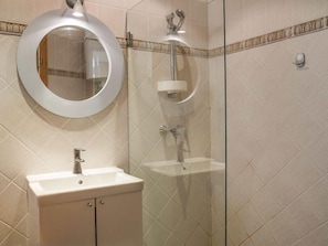 A bathroom with a round mirror, a sink, and a glass-enclosed shower area.