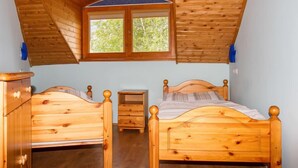 Una camera da letto con soffitto in legno a falde, due letti di legno, un piccolo comodino in legno e una finestra vista alberi.