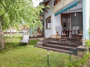 A patio with two striped chairs and a table, surrounded by a grassy area and a tree.