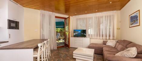 A modern living room with a wooden ceiling, a sofa, a TV, and a dining area with chairs and a table.