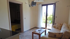 A compact living space with a kitchenette, a sofa, a table, and a sliding glass door leading to an outdoor area. - Stella Bay (Samos)