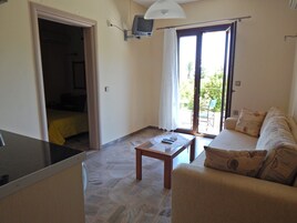 Un espacio habitable compacto con kitchenette, un sofá, una mesa y una puerta corrediza de vidrio que da a un área exterior.