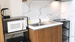A compact kitchen with wooden cabinets, a microwave, a sink, and a small refrigerator. - 8Adriatico2 Contemporary Luxurious Studio (Manila)