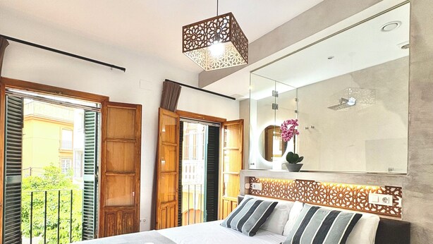 A modern hotel room with a large bed, a mirror, and a balcony with open shutters. - Unique House 5Br- Private SPA&POOL - StayInSeville (Sevilla)