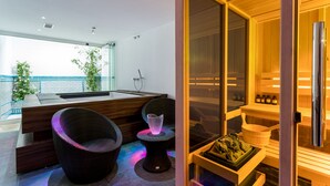 A modern spa area with a wooden reception desk, two wicker chairs, a small table, and a sauna room with a glass door. - Unique House 5Br- Private SPA&POOL - StayInSeville (Sevilla)