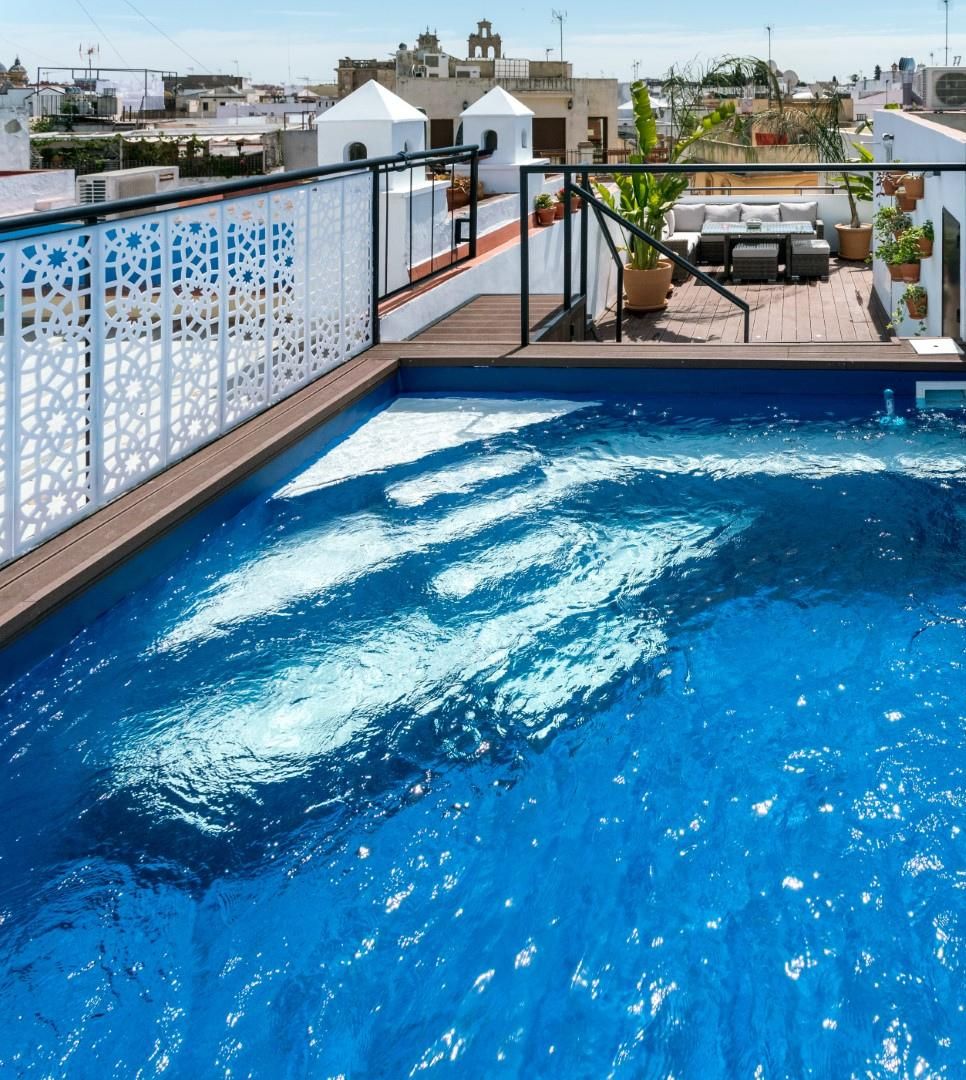 A rooftop swimming pool with a white decorative fence and a seating area with a table and chairs.
