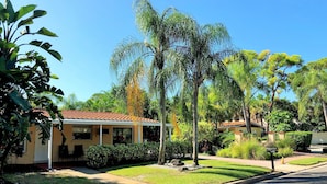Una casa residencial con techo de tejas, rodeada de céspedes cuidados y diversas plantas tropicales.