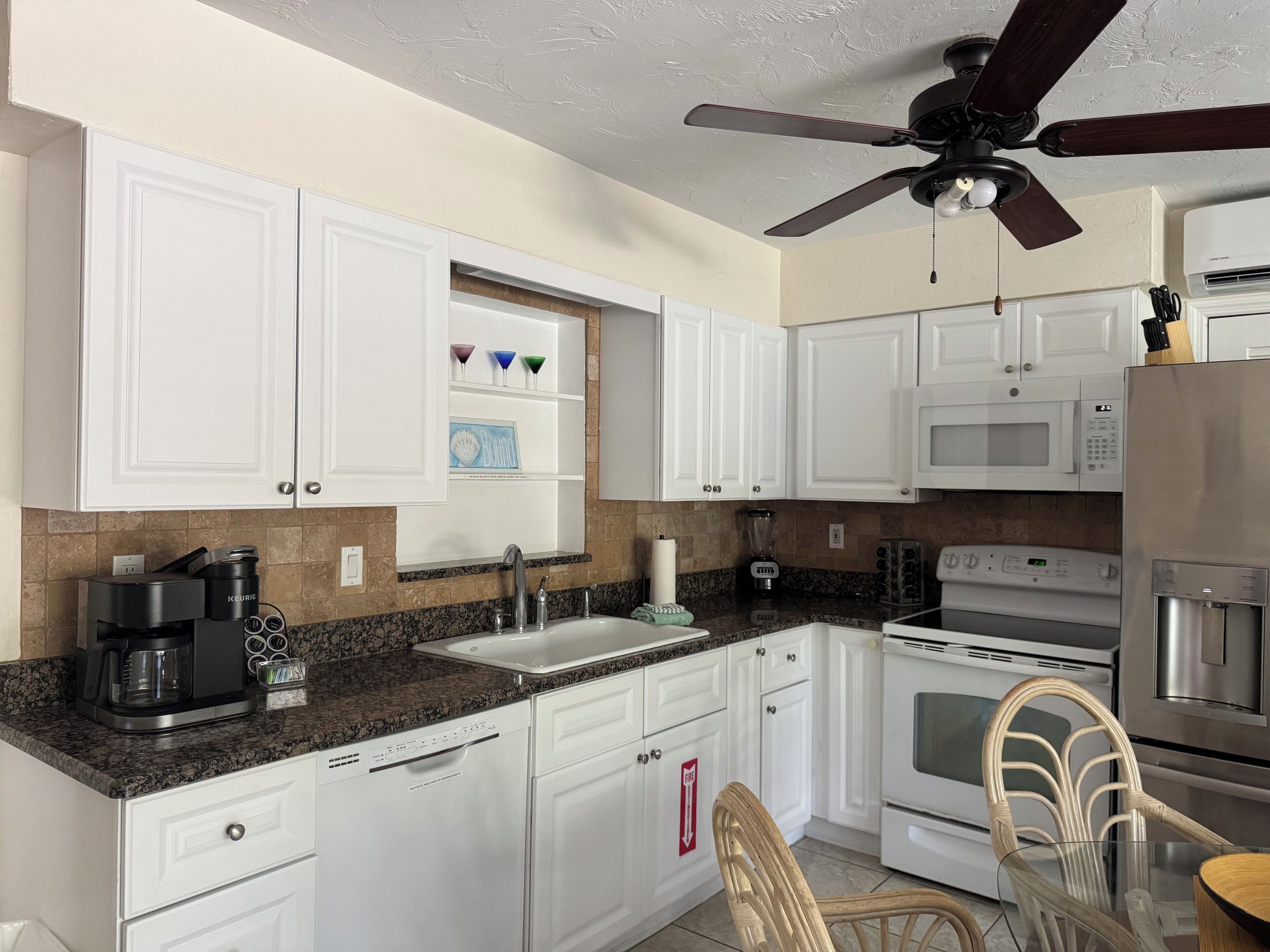 A kitchen with white cabinets, a granite countertop, a coffee maker, a microwave, an oven, and a ceiling fan.