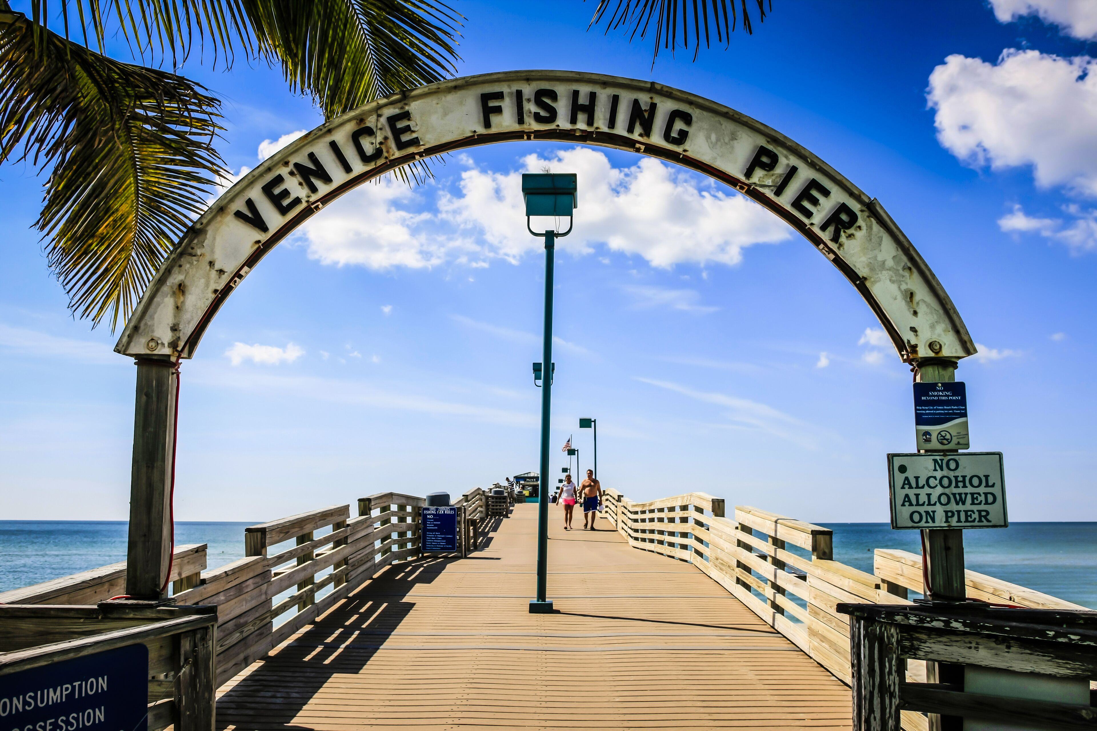 Un muelle de madera con un cartel que dice "Venice Fishing Pier" y un cartel que indica "No se permite el alcohol".