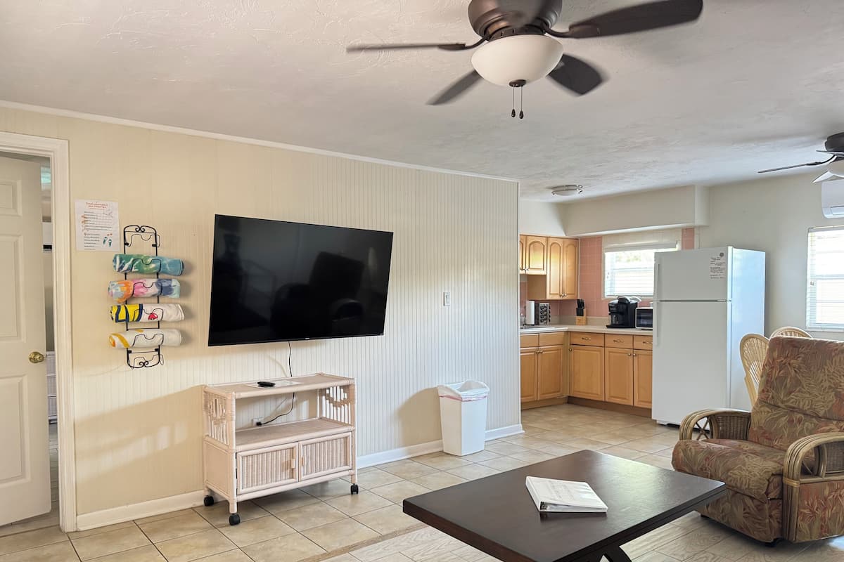 Una sala de estar con televisor de pantalla plana, muebles de mimbre, una mesa baja oscura y un ventilador de techo.