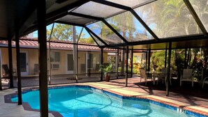 Una piscina con cerramiento de vidrio, rodeada de mobiliario de jardín y plantas.