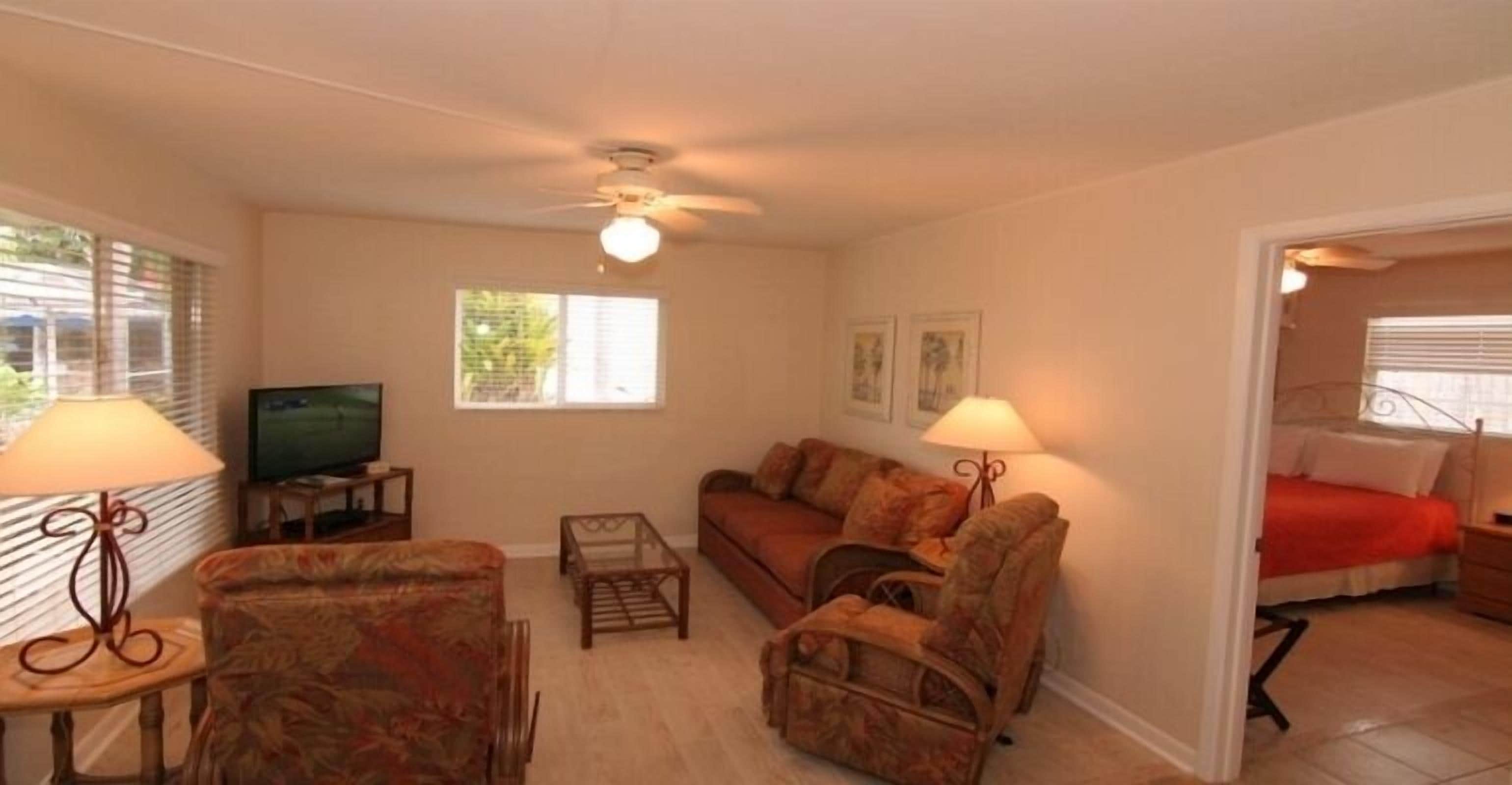 A living room with a sofa, armchairs, a television, and a ceiling fan.