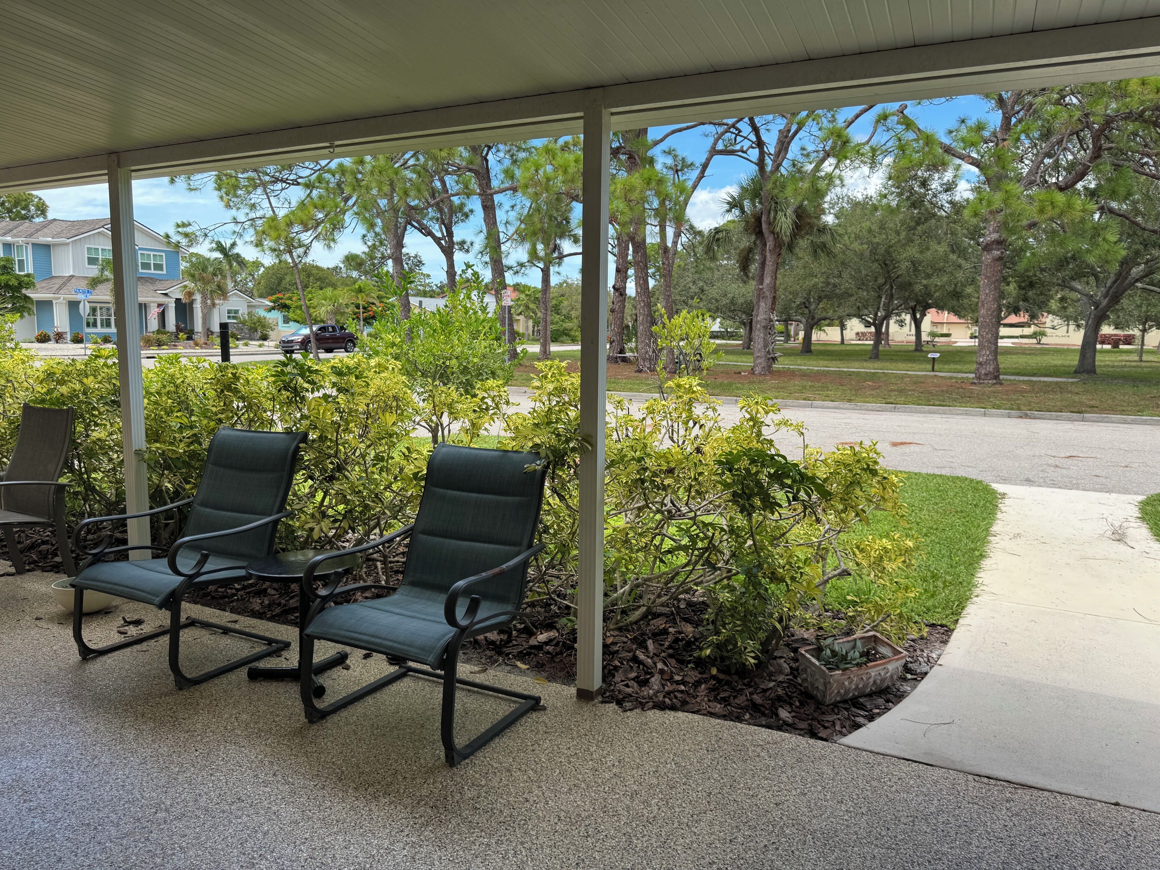 An outdoor seating area with two chairs and a table, surrounded by greenery and a view of a residential street.