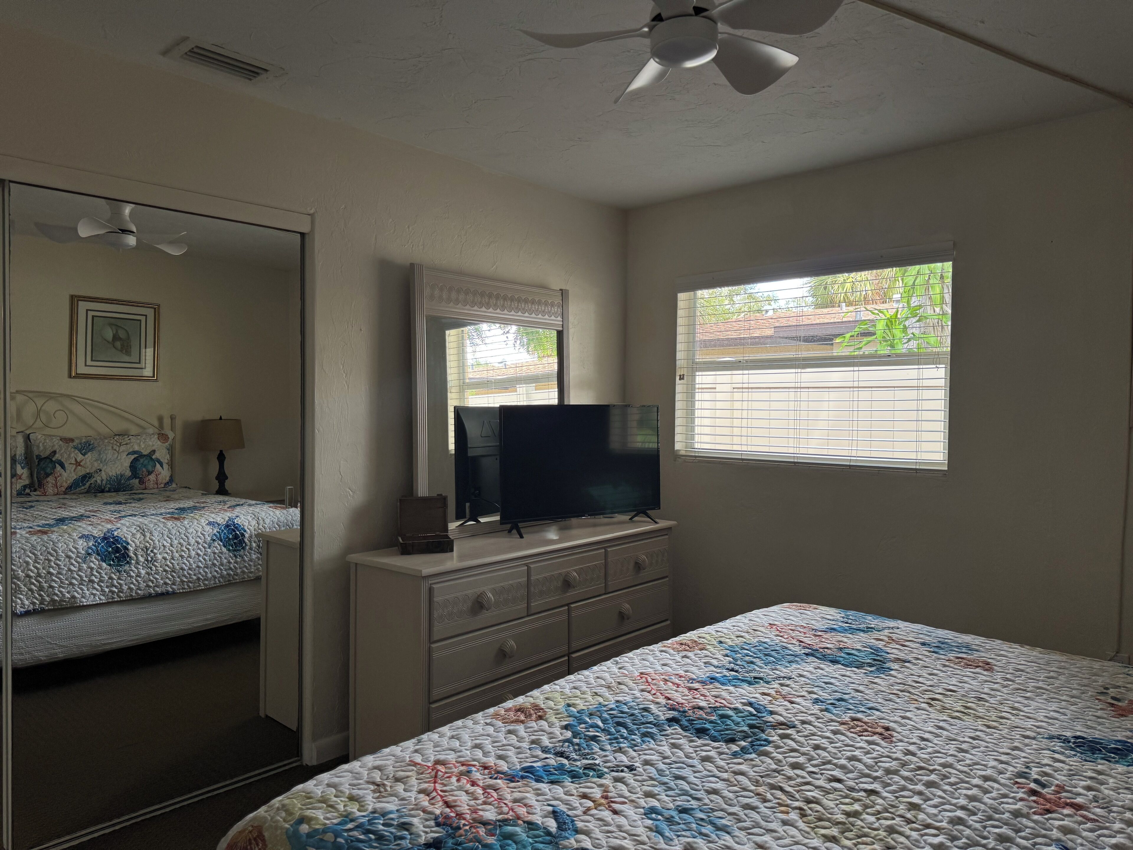 A bedroom with a bed, dresser, television, and a window with blinds.