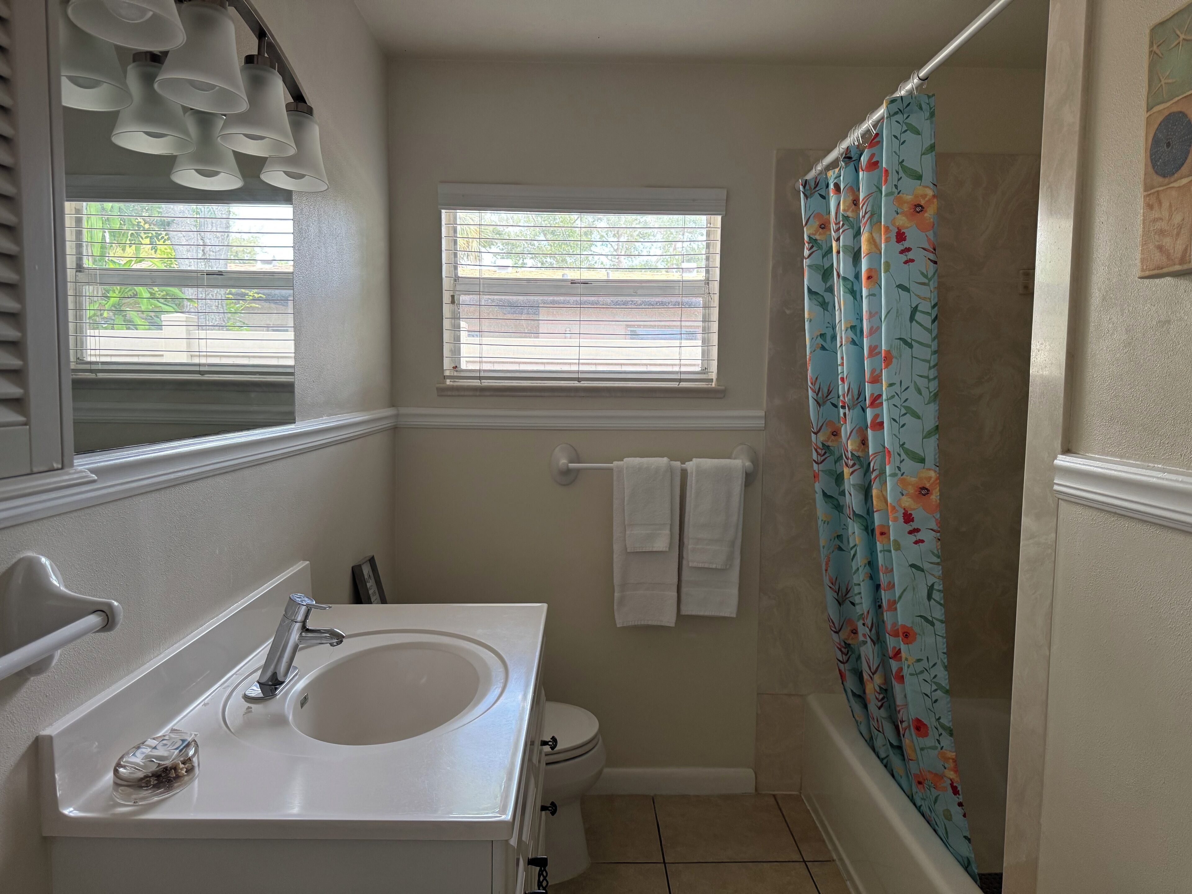 A bathroom with a white sink, a window with blinds, a toilet, and a shower curtain with a floral pattern.