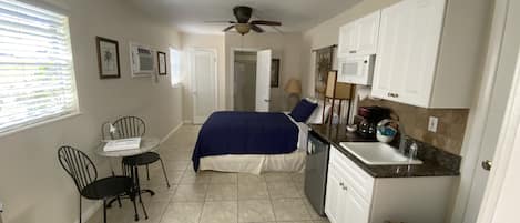 A compact hotel room with a bed, a small kitchenette, a dining area, and a bathroom.