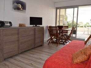A modern room with a wooden cabinet, a television, a dining table with chairs, and a bed with a red blanket.