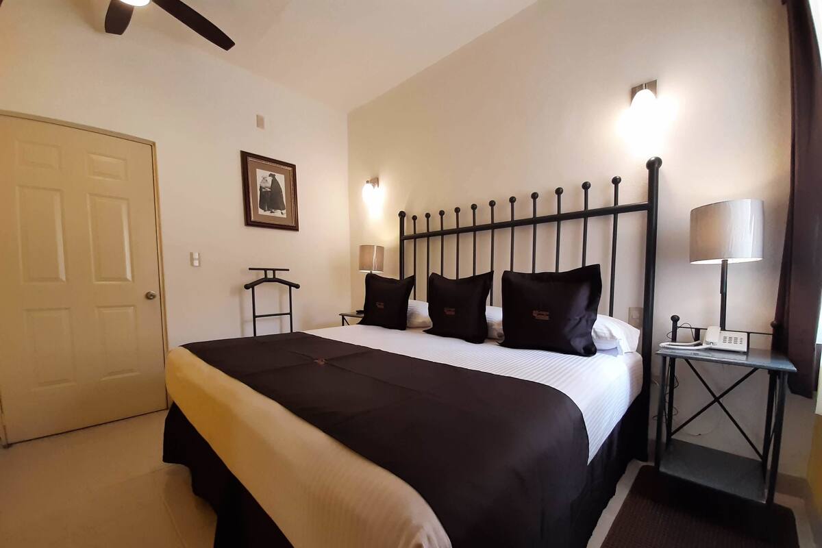 A hotel room with a bed, bedside tables, a lamp, a framed picture on the wall, and a door.