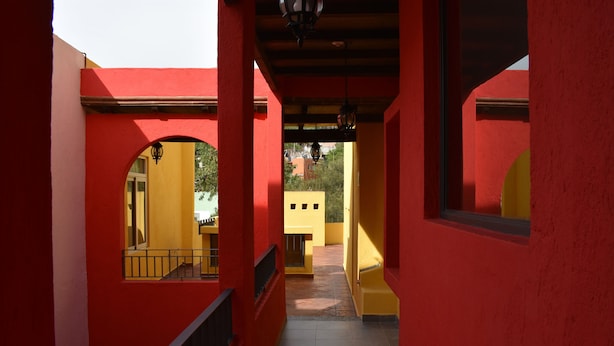 A corridor with red walls and yellow doors, leading to a balcony with a railing. - Real de la Presa (Guanajuato)
