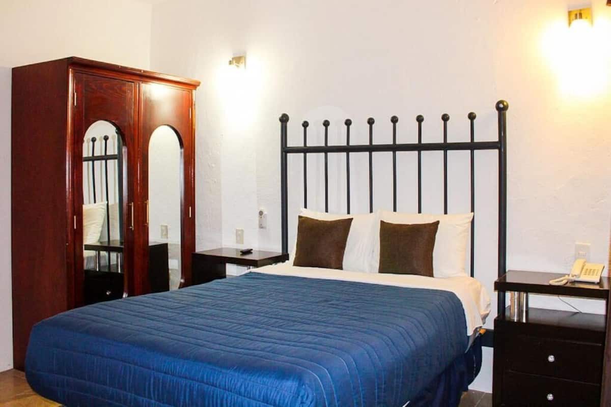 A bedroom with a bed, a wooden wardrobe, a nightstand, and a bedside table with a phone.