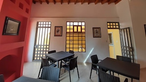 A dining area with a wooden ceiling, black tables, and chairs. There are windows with decorative grills and framed pictures on the walls. - Real de la Presa (Guanajuato)