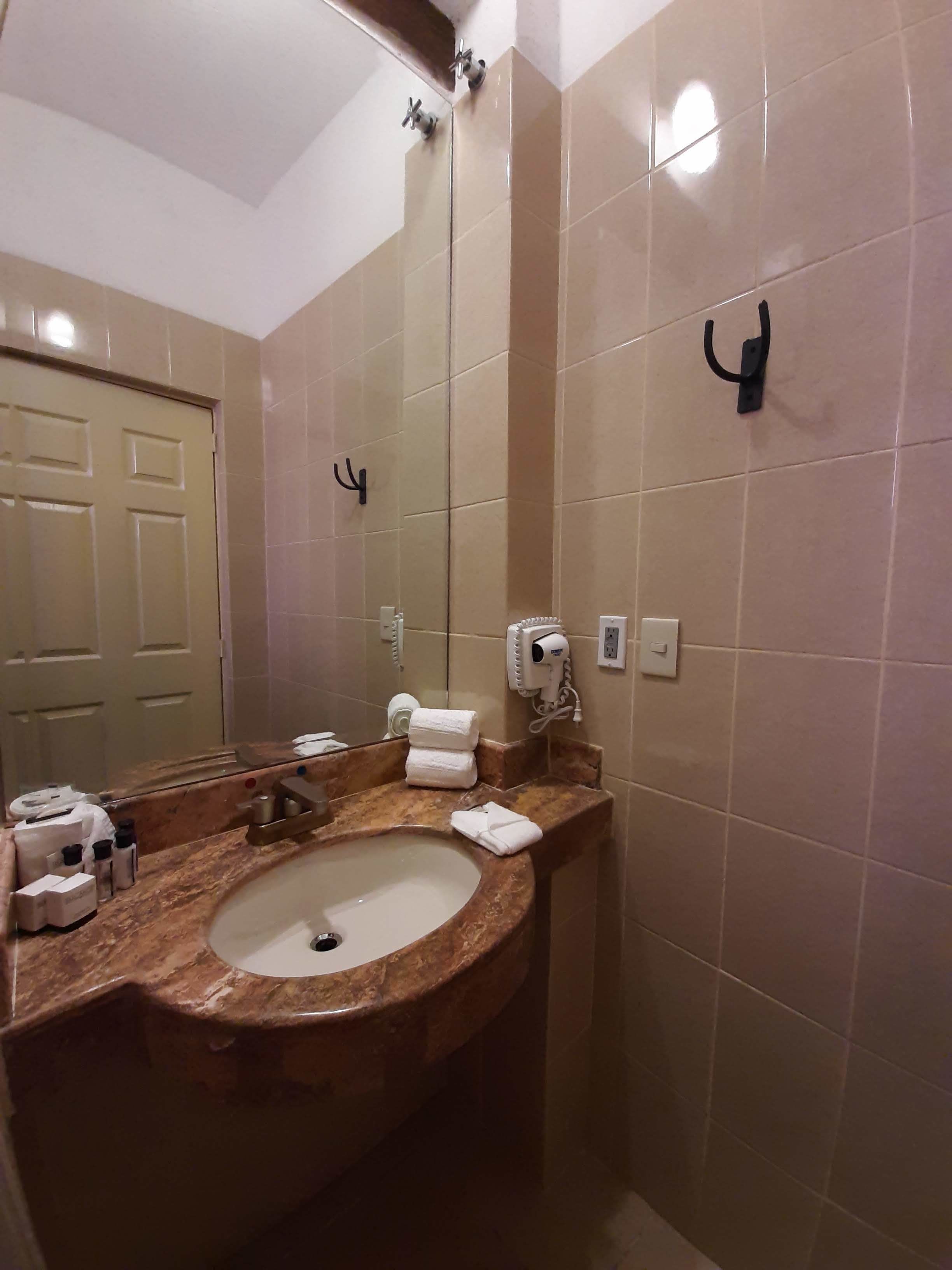 Une salle de bain avec un lavabo en marbre, un grand miroir, un porte-serviettes et un sèche-cheveux fixé au mur.