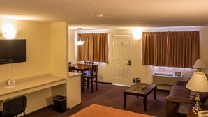 Habitación de hotel con televisión de pantalla plana, un escritorio, una mesa de comedor con sillas, un sofá, una mesa de centro, una lámpara y un equipo de aire acondicionado.