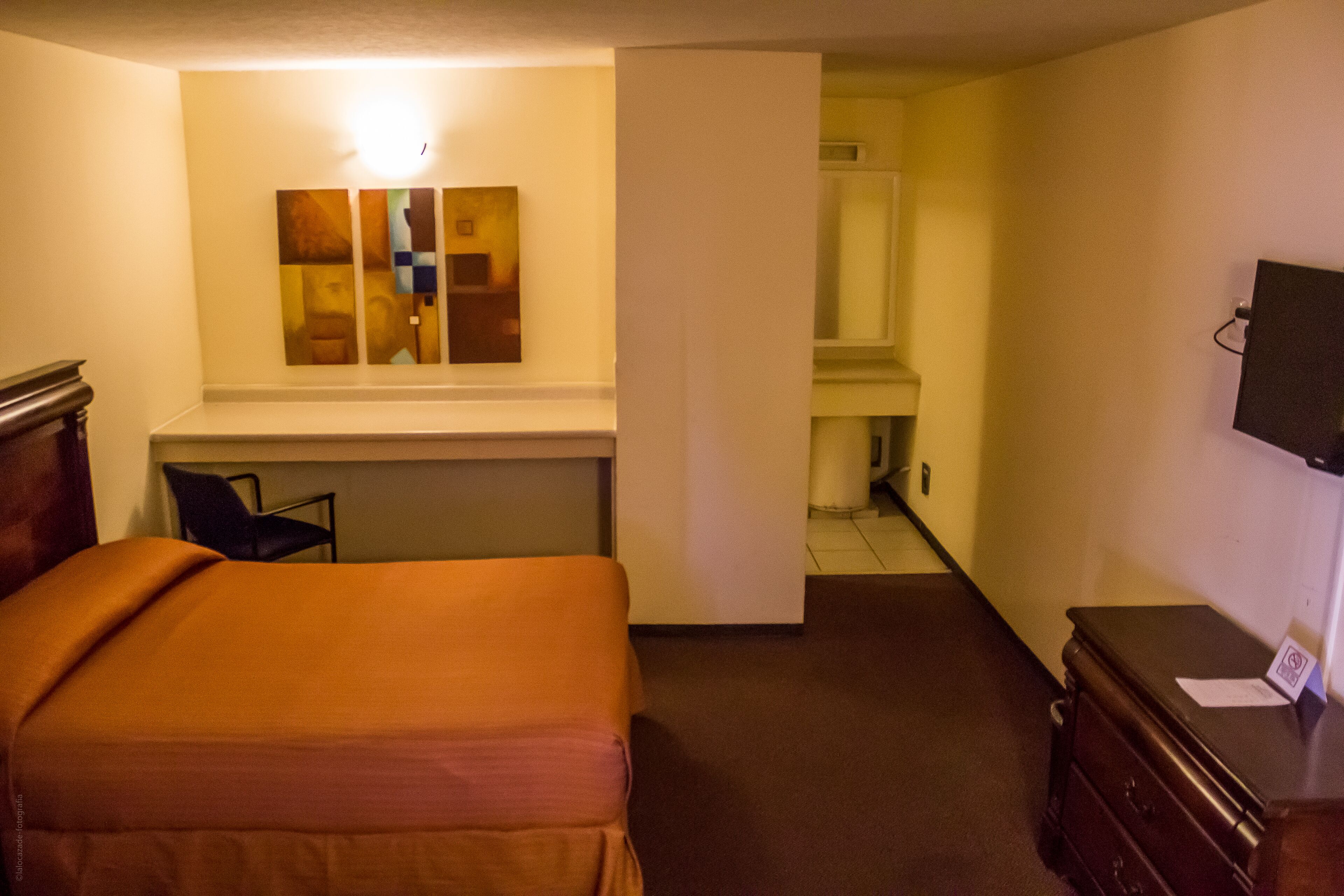 Una habitación de hotel con cama, escritorio, silla, cómoda y televisor.