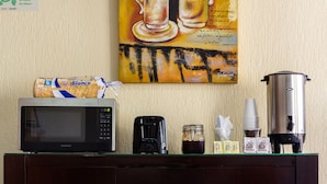 Una kitchenette con microondas, cafetera y jarra para café sobre un mueble de madera.