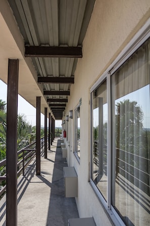 A covered corridor with large windows, concrete flooring, and metal beams.