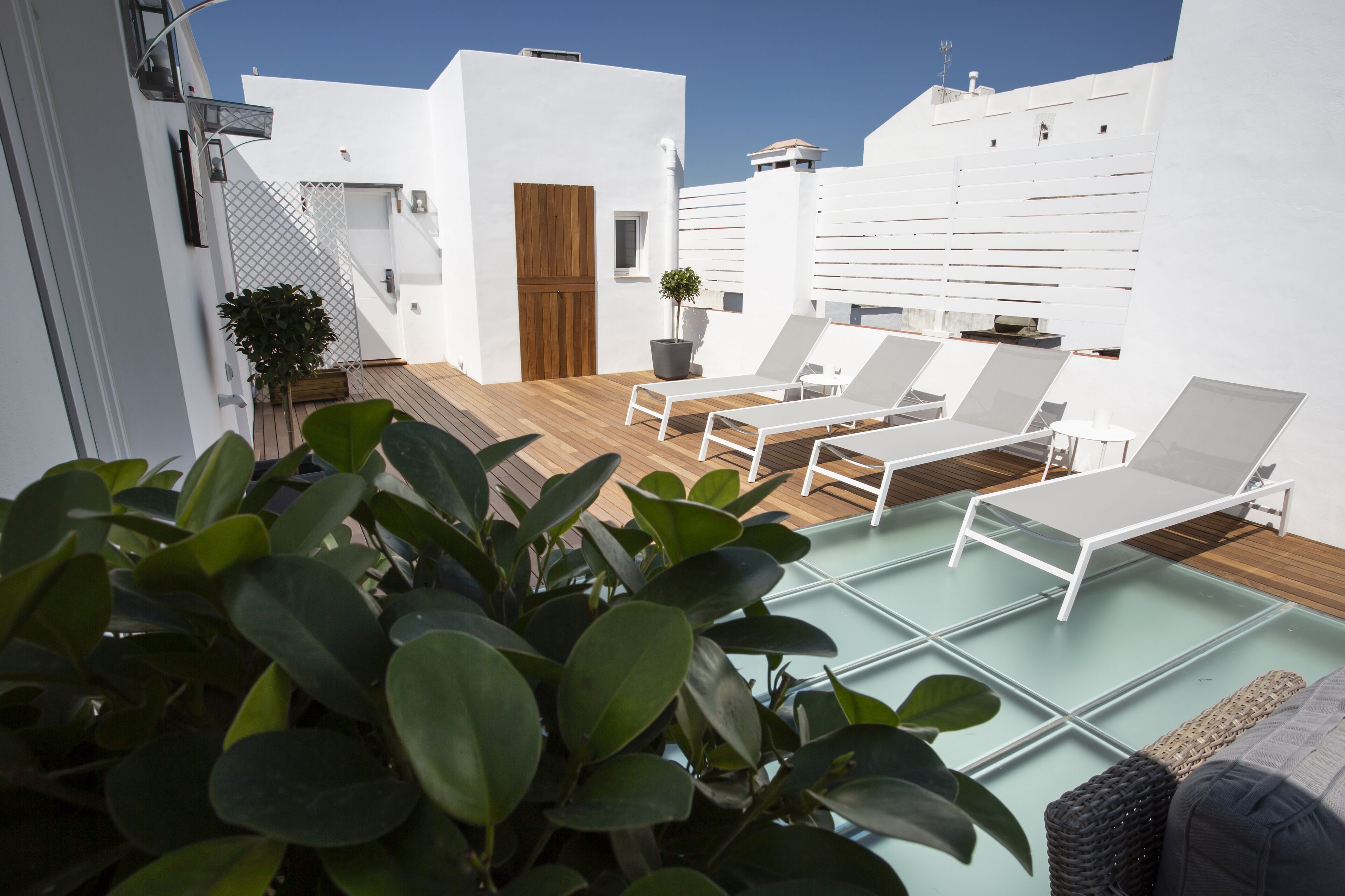 A rooftop terrace with white walls, a wooden deck, and two lounge chairs.