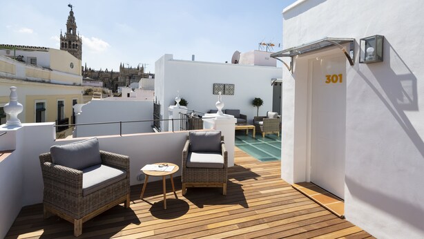 Una terraza en la azotea con mobiliario de mimbre, una pequeña mesa y una puerta con el número 301.